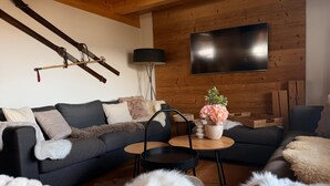 A modern living room with a grey sofa, a coffee table, and a TV mounted on a wooden wall.