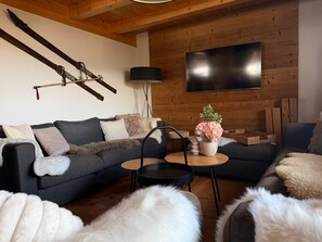 Un salon moderne avec un canapé gris, une table basse et un téléviseur fixé à un mur en bois.