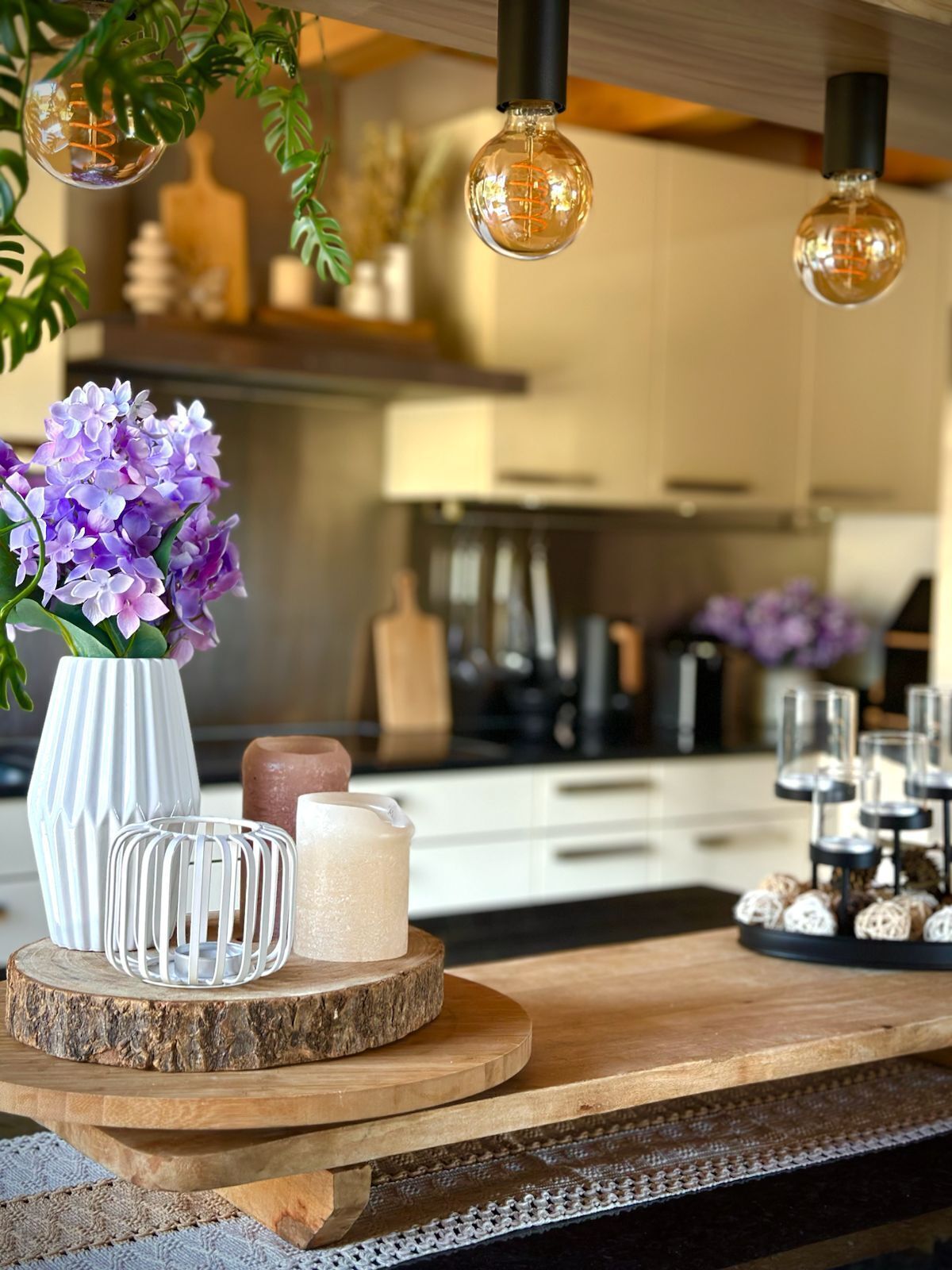 A kitchen counter with a vase of purple flowers, a candle, and a glass candle holder.