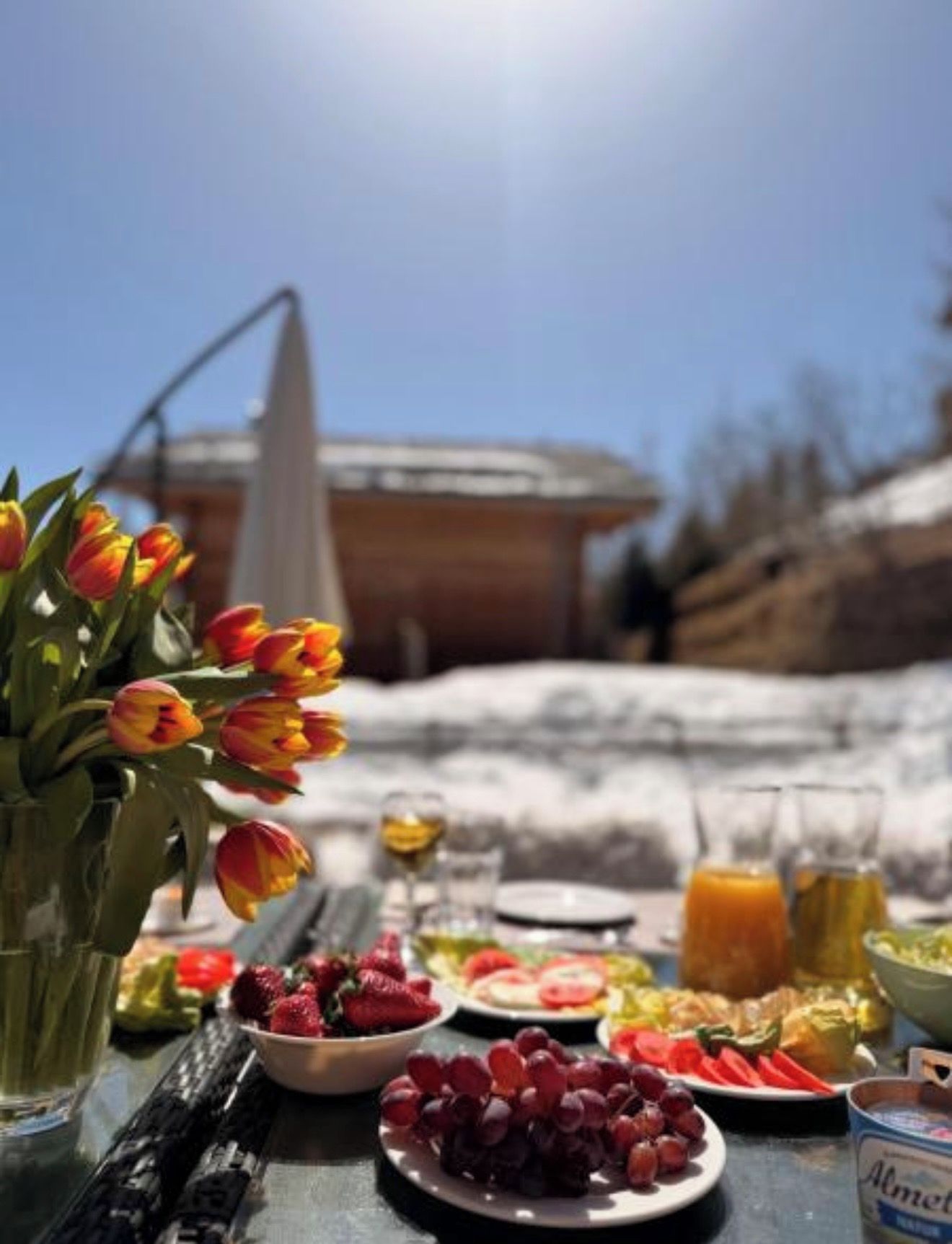 A table set outdoors with food and drinks, a vase of tulips, and a clear sky.