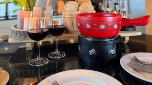 A dining table with candles, wine glasses, a red pot, and bread.