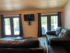 Ein Wohnzimmer mit einer Ledersofa, einem flachbildfernseher an der Wand und einer Glasschiebetür, die zu einem Außenbereich führt.