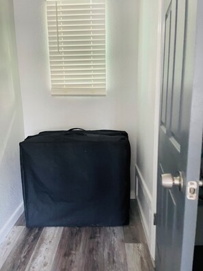 Una habitació amb sòl de fusta, una porta tancada i una finestra amb persianes.