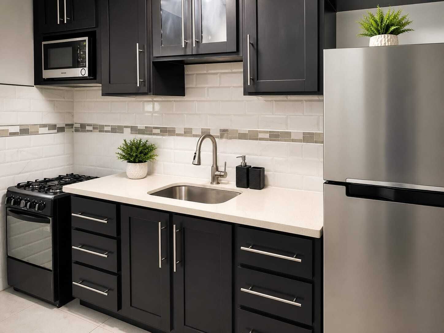 A modern kitchen with black cabinets, a stainless steel refrigerator, a microwave, and a sink with a faucet.