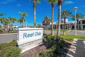 Schild für Reef Club, in der Nähe ein Stoppschild, Palmen und im Hintergrund ein modernes Gebäude.