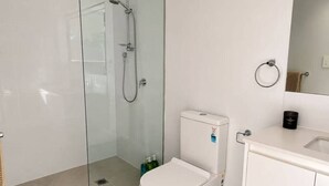 A modern bathroom with a glass-enclosed shower, a white toilet, and a sink with a mirror above it. - No.20 3B Pimpama Home (Pimpama)