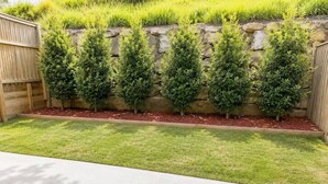A backyard with a stone wall, a wooden fence, and a well-maintained lawn. - No.20 3B Pimpama Home (Pimpama)