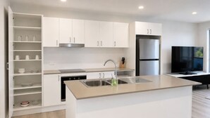 A modern kitchen with white cabinetry, a stainless steel refrigerator, a built-in oven, and a large island with a sink. - No.20 3B Pimpama Home (Pimpama)