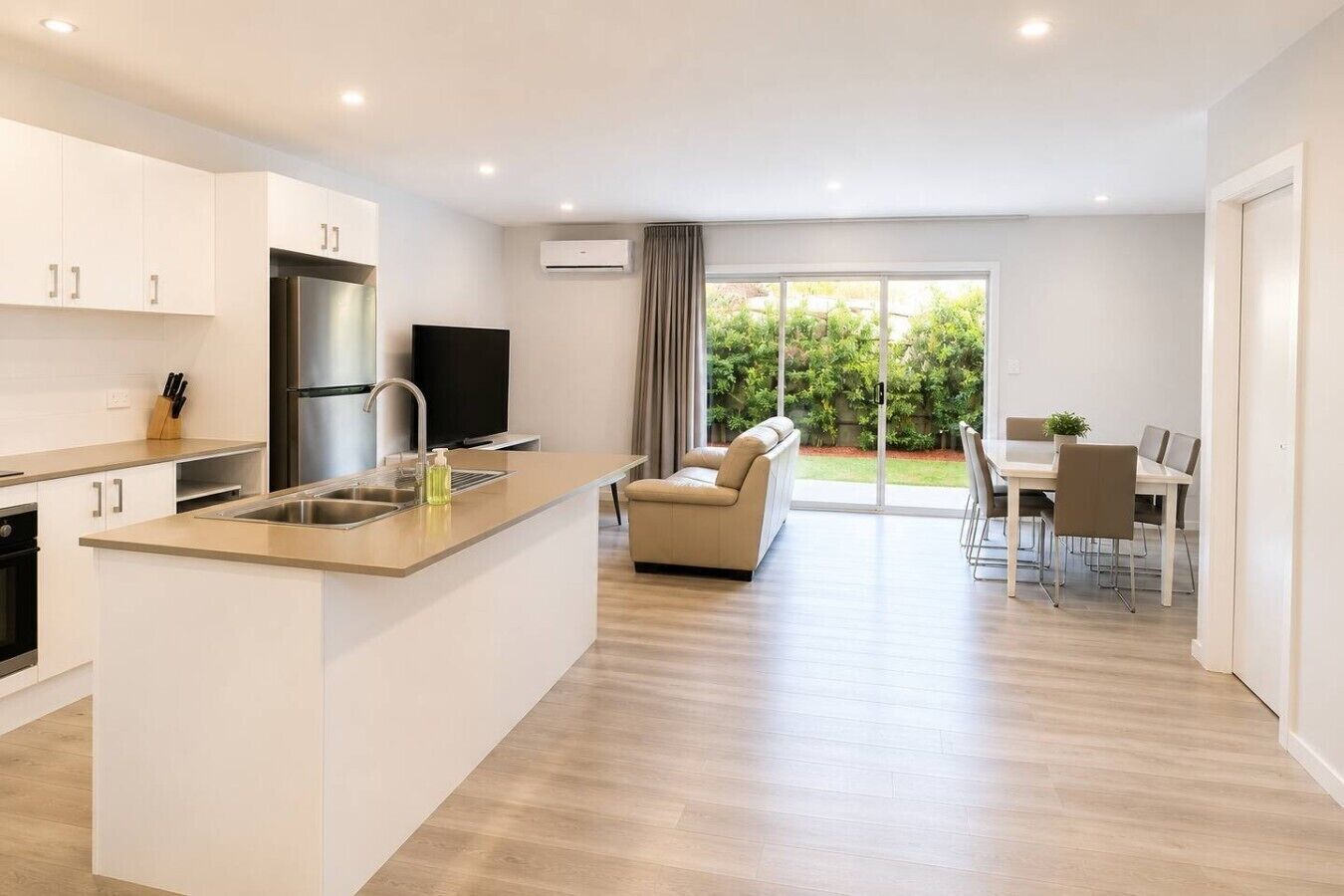 Een moderne keuken met een centraal eiland, een eethoek met tafel en stoelen, en een zithoek met bank en televisie.