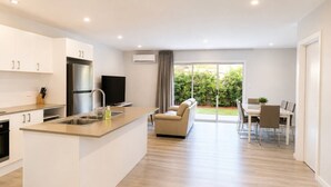 A modern kitchen with a central island, a dining area with a table and chairs, and a living space with a sofa and a TV. - No.20 3B Pimpama Home (Pimpama)