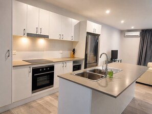 Une cuisine moderne dotée d’appareils électroménagers en acier inoxydable, d’un îlot central avec un évier et d’un four encastré.