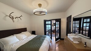 Et hotelværelse med en stor seng, et træsengegærde, en loftlampe, et spejl og udsigt til det frie gennem en glasdør.