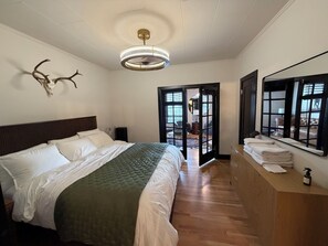 A hotel room with a large bed, a wooden headboard, a ceiling light fixture, a mirror, and a view of the outside through a glass door. - Apartment Eight: Historic Pendleton; Walk to Round-Up, HC, Dining & More. (Pendleton)