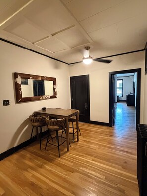 Un comedor con una mesa y sillas de madera, un ventilador de techo y una puerta que da a otra habitación.