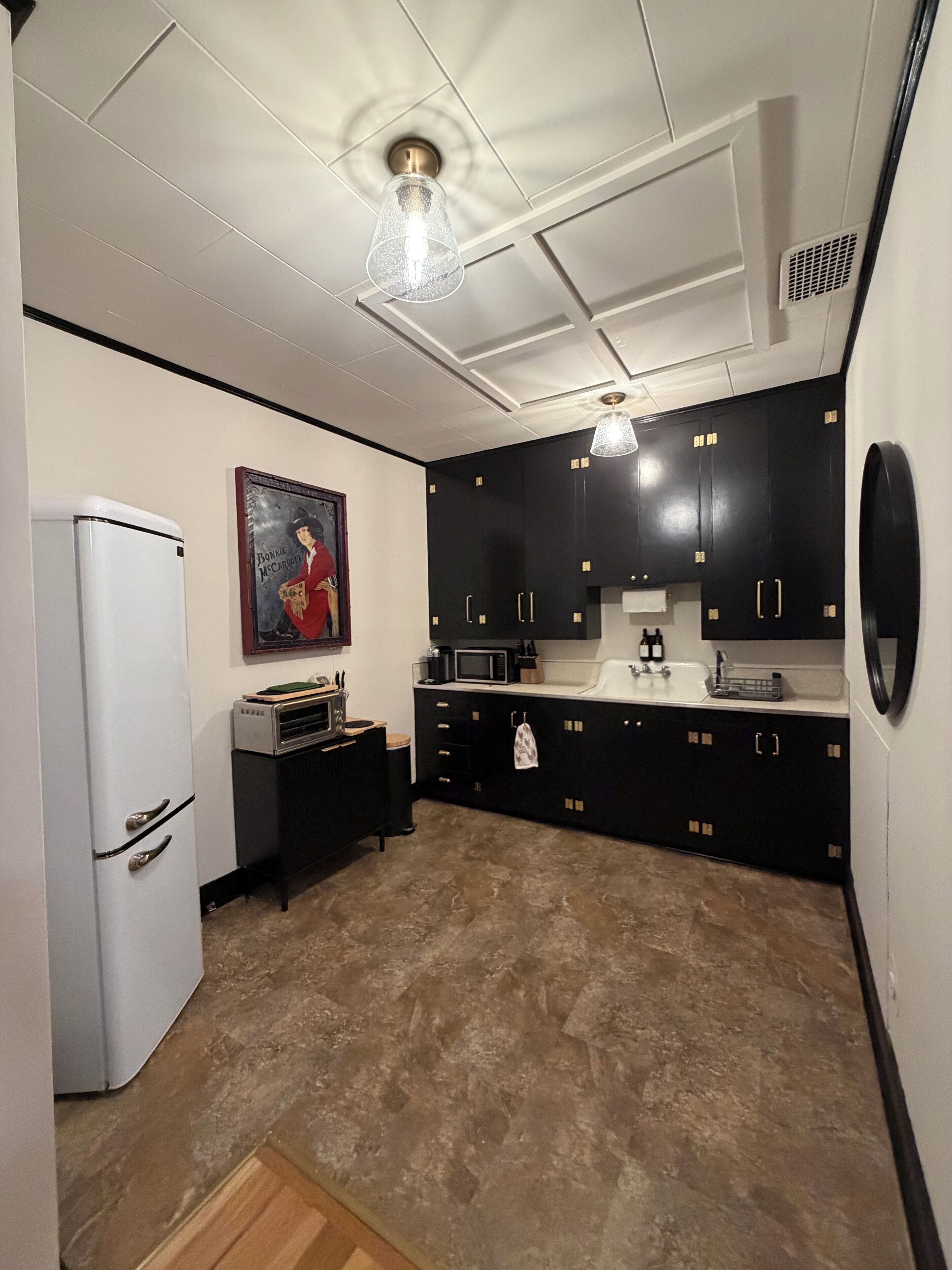A kitchen with black cabinets, a white refrigerator, a microwave, and a sink.