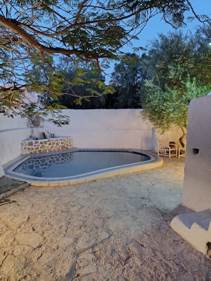 Piscina con baldosas de piedra, rodeada por una zona de arena y un muro bajo.