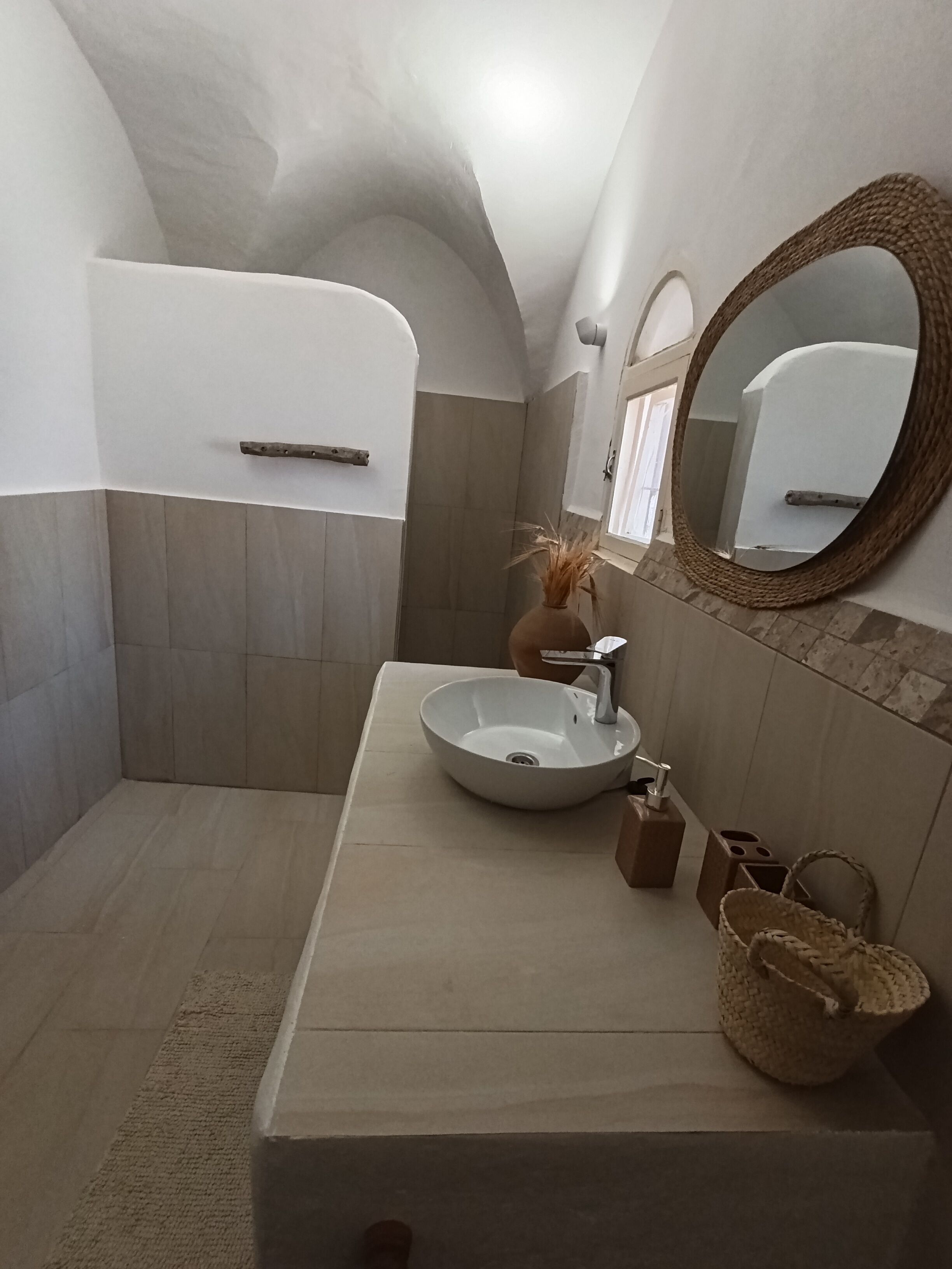 Une salle de bain avec un lavabo blanc, un miroir rond et un panier en osier.