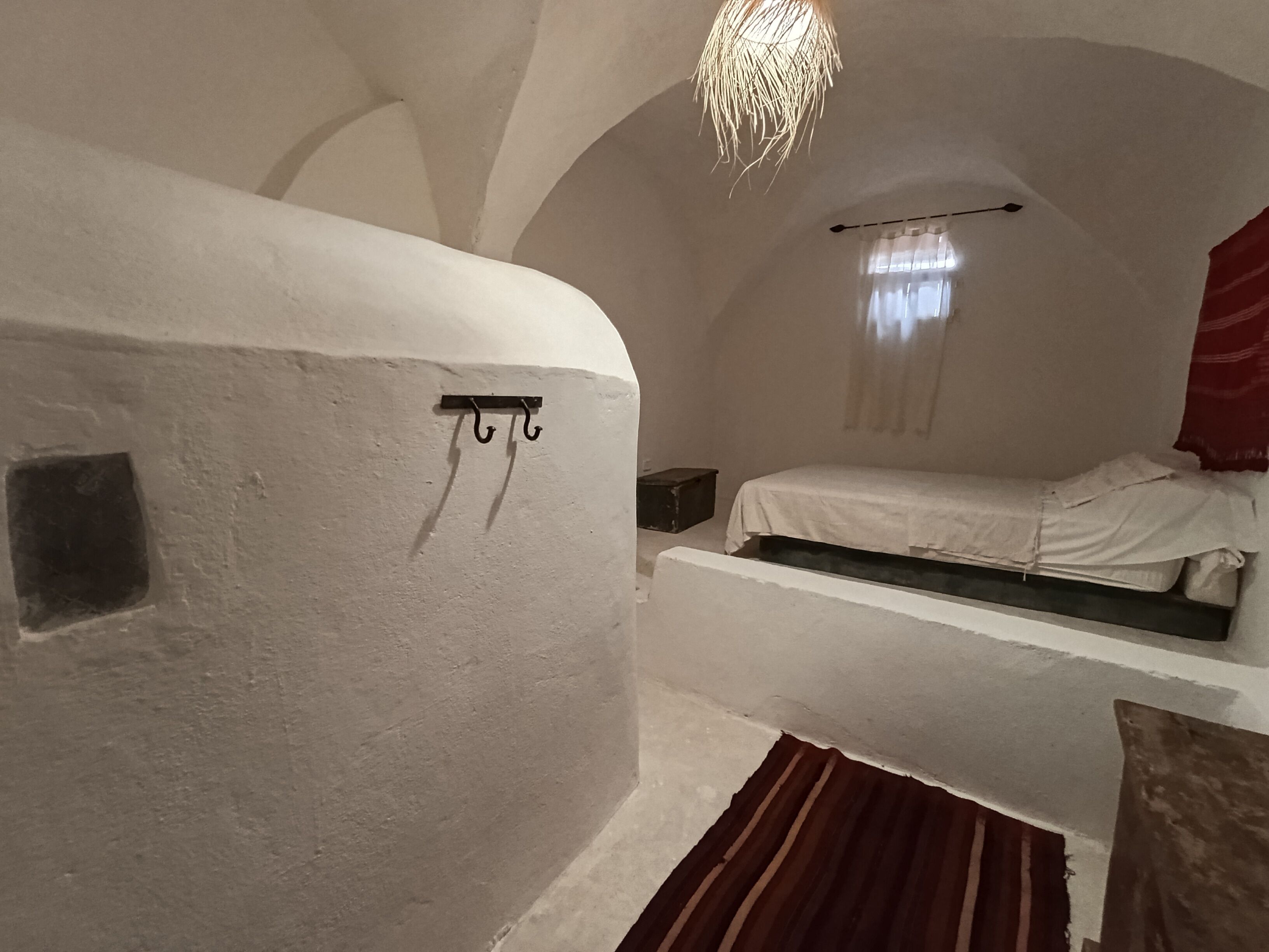 A room with a bed, a hanging light fixture, and a small shelf.