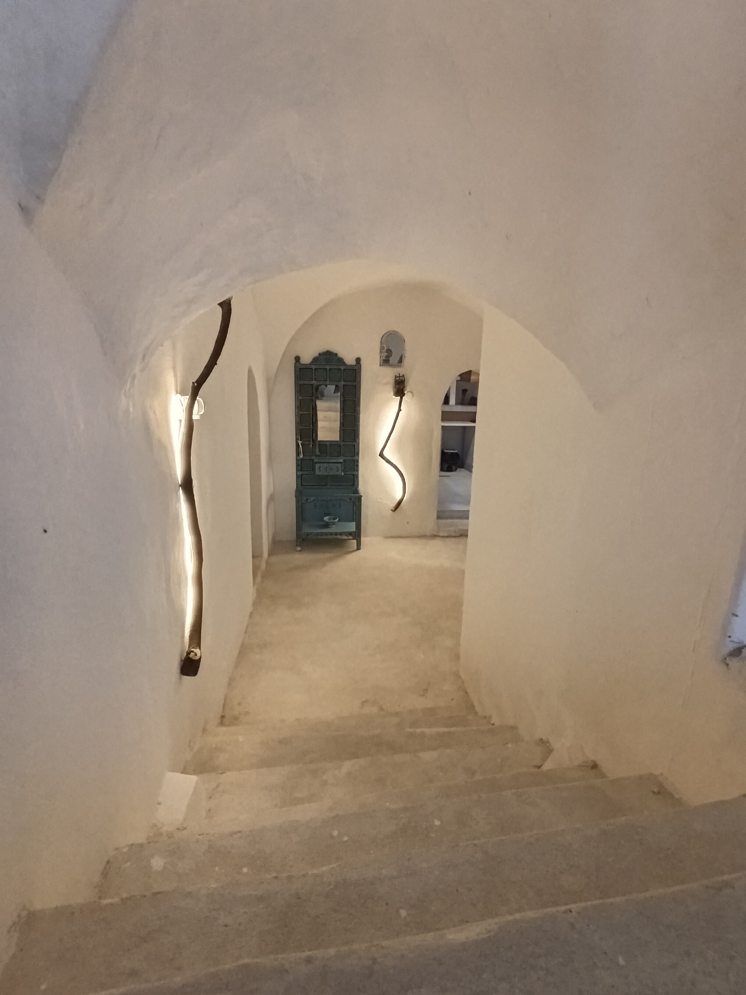 Una stretta scala ad arco conduce a una stanza con una porta verde, un tavolino e una sedia.
