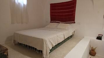 Ein Schlafzimmer mit einem Einzelbett, einer Bank, einem Fenster mit Vorhängen und einem roten Wandteppich.