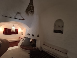 Una habitación con un banco de piedra, una lámpara colgante y un pequeño ventanal de arco con adornos.