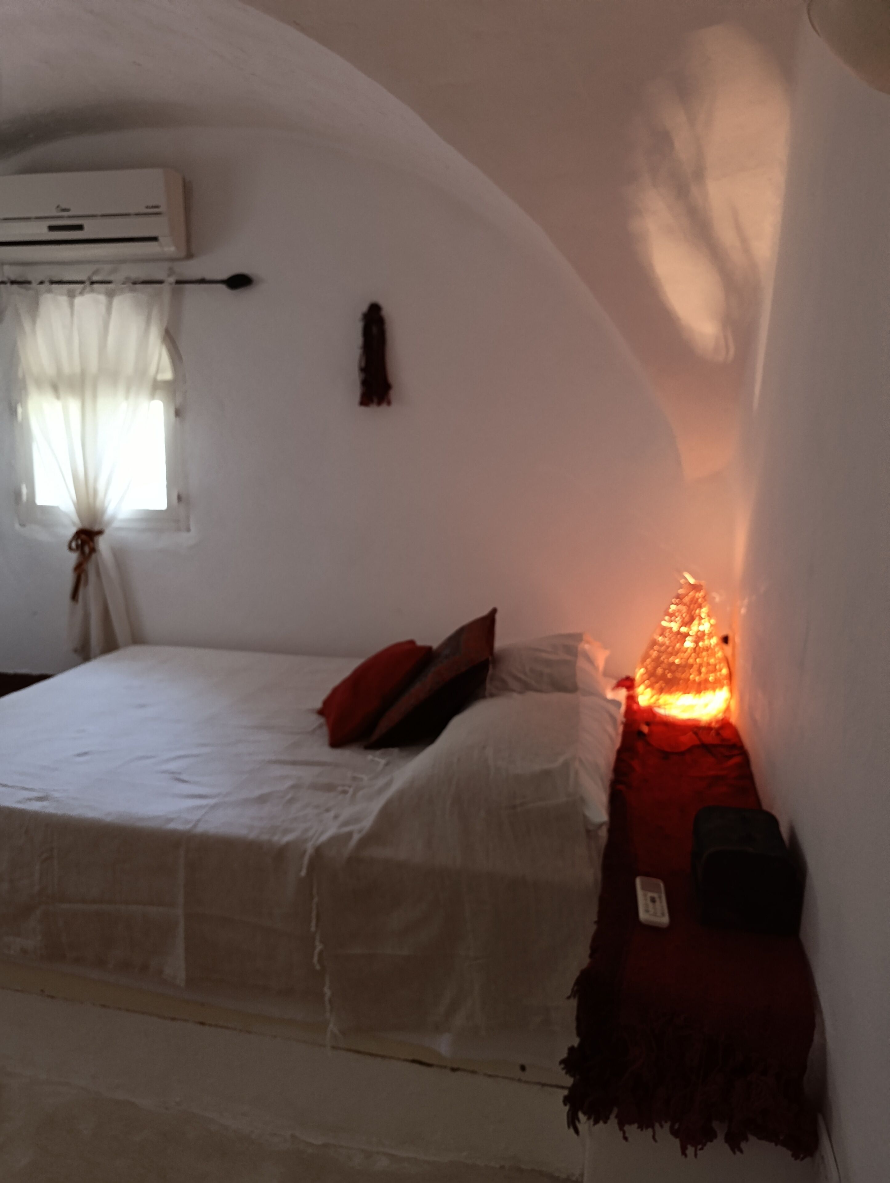 Una camera da letto con un letto, un comodino, un condizionatore d'aria a muro e una finestra con tende.