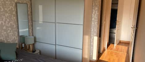 A bedroom with a bed, bedside lamps, a wardrobe, and a view of a hallway leading to a door.