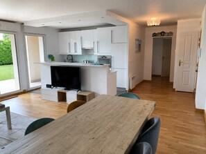 Una cocina moderna con armarios blancos, horno empotrado y comedor con mesa y sillas de madera.
