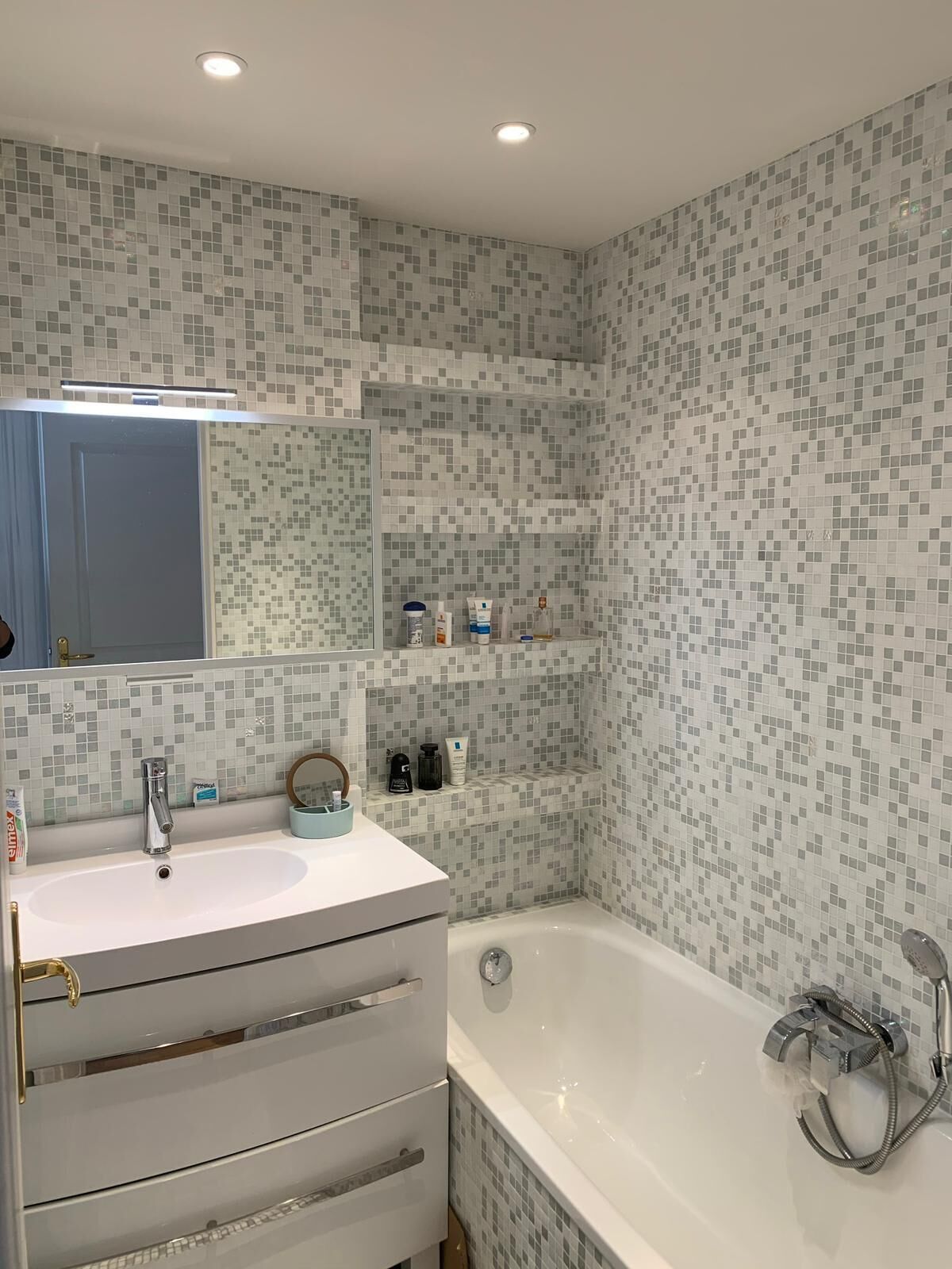 Un baño con lavamanos blanco, espejo, bañera y paredes con azulejos.