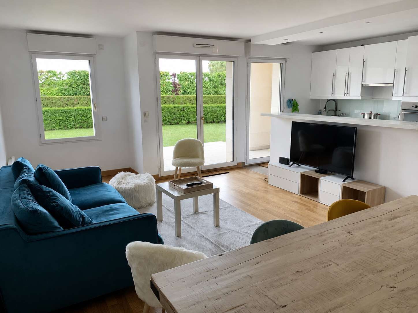 A modern living room with a blue sofa, a white fluffy chair, a wooden coffee table, and a TV.