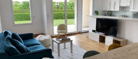 A modern living room with a blue sofa, a white fluffy chair, a wooden coffee table, and a TV.