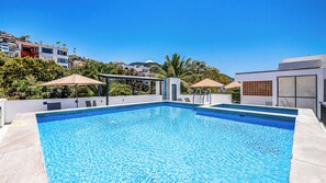 Una piscina rectangular con superficie de agua azul cristalina, rodeada por un solárium blanco.