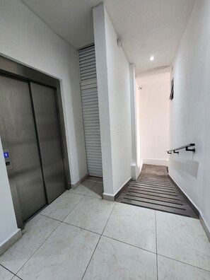 Un pasillo con piso de baldosas, un ascensor cerrado y una escalera que sube a otro nivel.