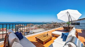 A balcony with a view of the sea, a white umbrella, and outdoor furniture. - Huge Private Terrace - Panoramic Bay Views - Walk to the Malecón (Puerto Vallarta)