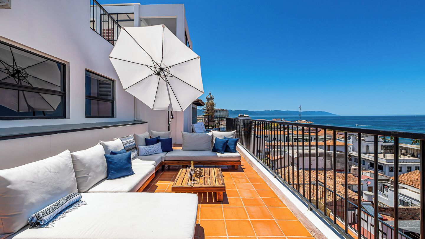 A balcony with a white sofa, a wooden coffee table, and a white umbrella.
