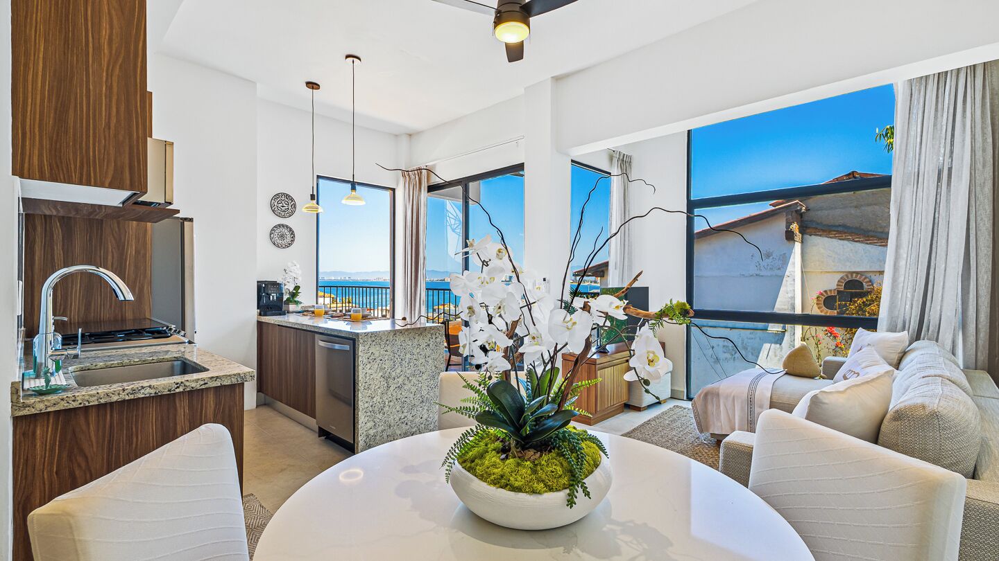 A modern interior with a kitchen, dining area, and living space, featuring a large window with a view.