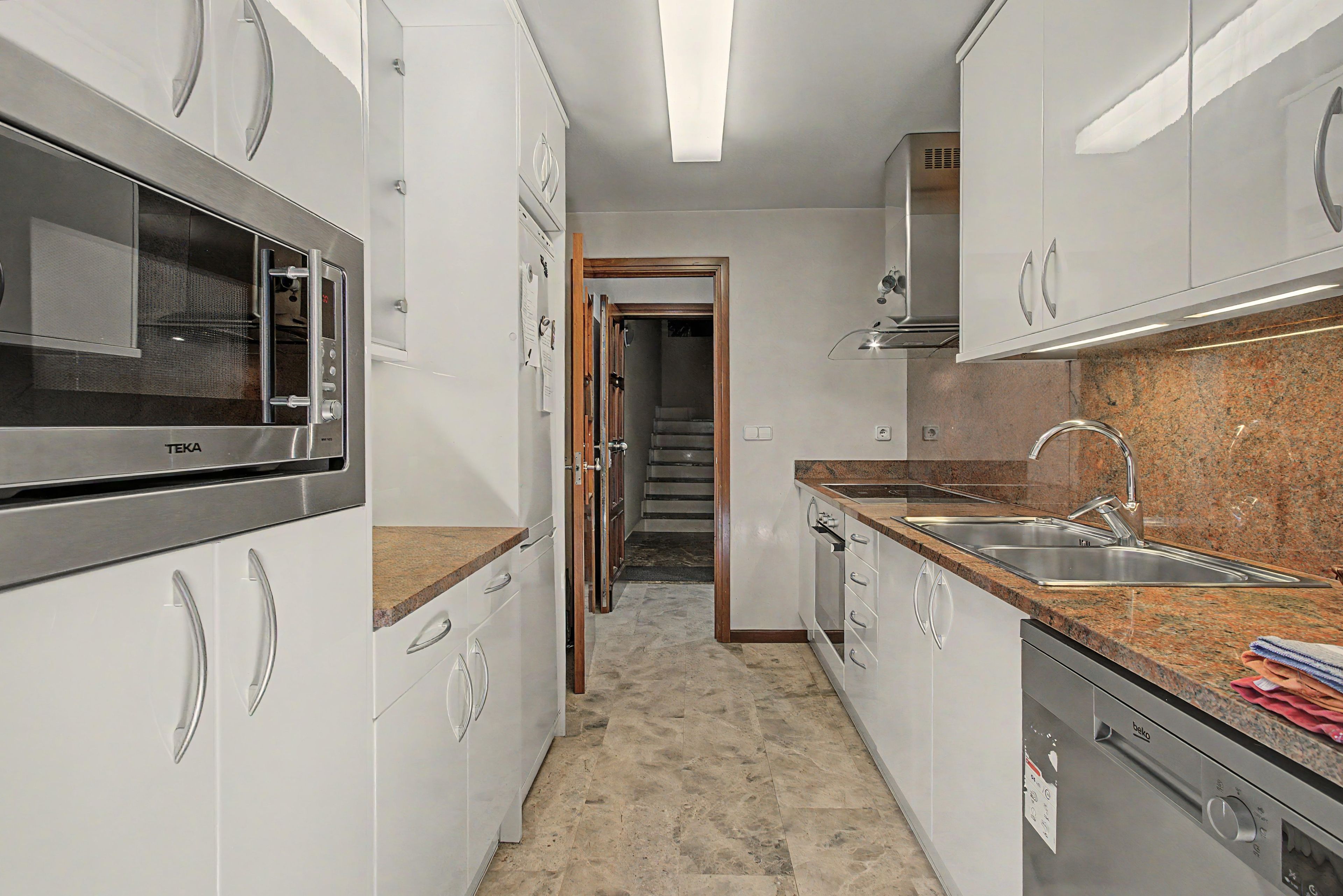 Een moderne keuken met roestvrijstalen apparatuur, granieten aanrechtbladen en witte kastjes.