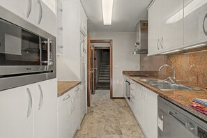Ett modernt kök med vitvaror i rostfritt stål, bänkskivor i granit och vita köksluckor.