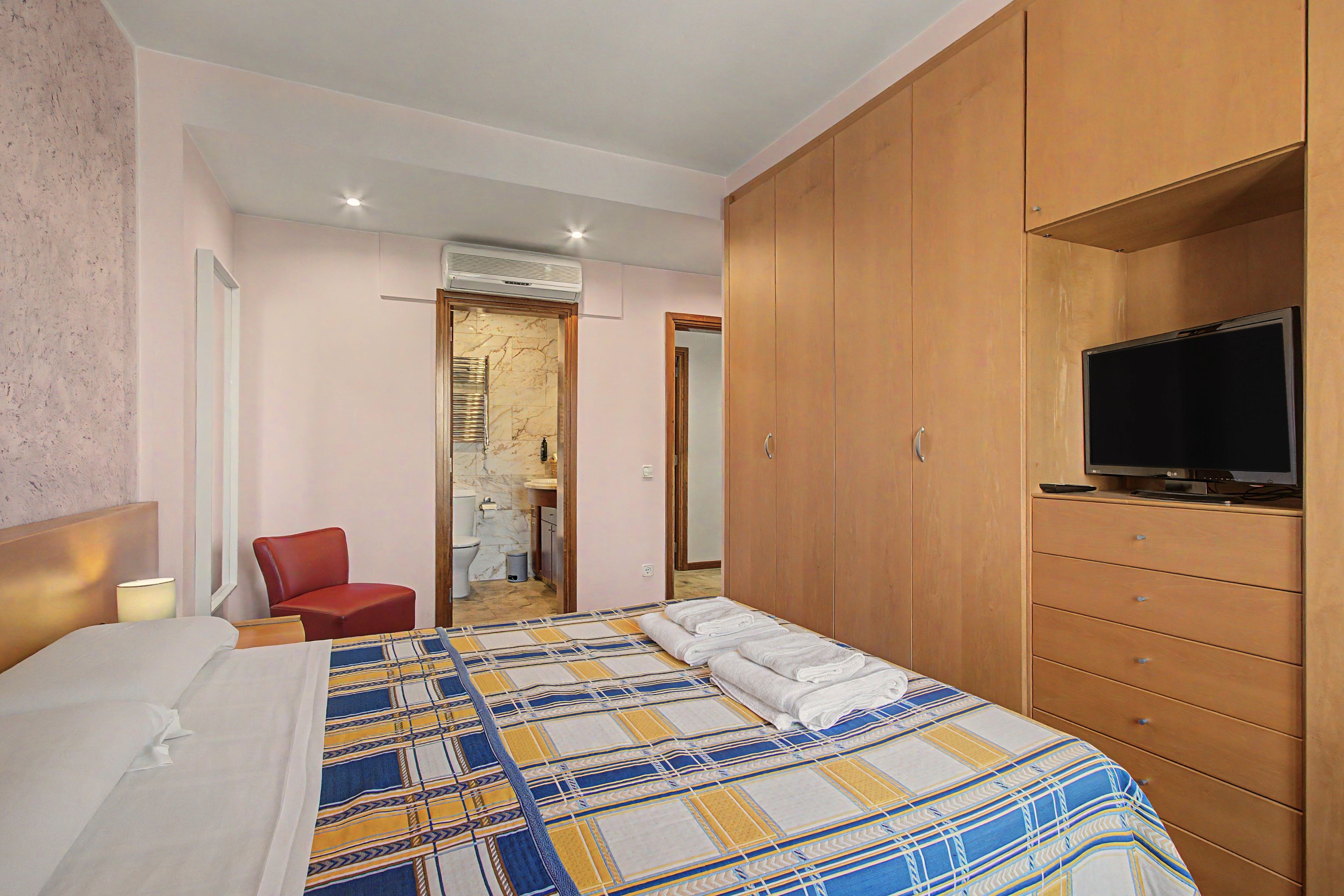 Habitación de hotel con cama, televisión, armario y baño visible a través de una puerta abierta.