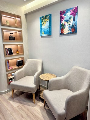 Una habitación con dos sillones, una mesa redonda pequeña y una estantería con diversos objetos.