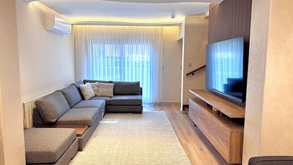 Una sala moderna con un sofá modular, un televisor de pantalla plana y un mueble de entretenimiento de madera.