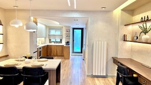 Una cocina moderna con armarios de madera, un comedor con una mesa para dos, y vista hacia la sala de estar.