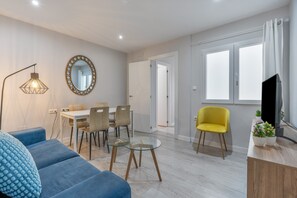 A modern living room with a sofa, a dining table with chairs, a yellow armchair, a TV, and a large window with curtains. - Triviño Granada Centro Apartment with Wi-Fi, Air Conditioning and Optional Parking (Granada)