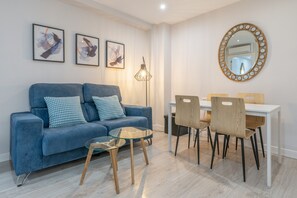 A modern living room with a blue sofa, glass coffee table, and a dining area with wooden chairs and a white table. - Triviño Granada Centro Apartment with Wi-Fi, Air Conditioning and Optional Parking (Granada)