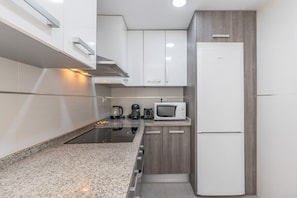 A compact kitchen with white cabinets, a built-in microwave, a coffee maker, and a stainless steel range hood. - Triviño Granada Centro Apartment with Wi-Fi, Air Conditioning and Optional Parking (Granada)