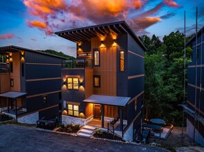 A modern multi-story building with a covered outdoor seating area and a well-lit entrance. - Next Play Clubhouse | Waterpark Resort & Game Room (Sevierville)