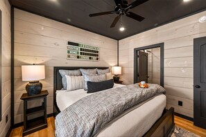 Une chambre à coucher comprenant un lit, deux tables de chevet avec des lampes, un ventilateur de plafond et un panneau mural avec des chiffres.
