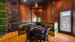 Una habitación con pared de ladrillo, una mesa con sillas y una ventana con persianas.