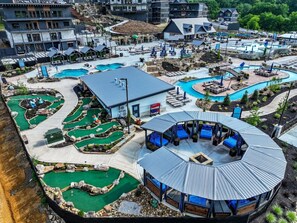 Ein Golfplatz mit mehreren Putting-Greens, einem zentralen Pavillon mit Sitzgelegenheiten und einem Poolbereich mit Liegestühlen.
