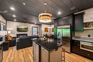 A modern kitchen with a central island, stainless steel appliances, and a dining area with a fireplace. - Next Play Clubhouse | Waterpark Resort & Game Room (Sevierville)